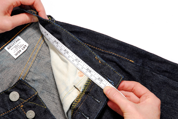 Measuring waist of denim jeans with tape measure.